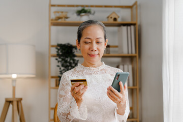 Happy mature asian woman using credit card and mobile phone for shopping on internet, cashless...