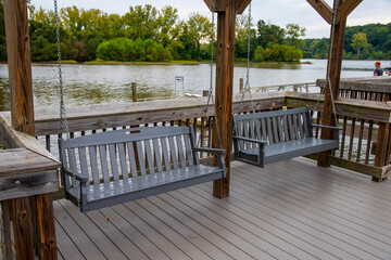 two gray wooden swings hanging from chains on a brown wooden deck over the Catawba River surrounded...