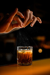 close-up view on male fingers holding zest and splashing on old-fashioned glass with cocktail