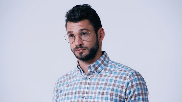 pensive nerd in checkered shirt and eyeglasses looking away isolated on grey.