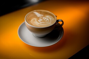 close-up view on white cup of coffee drink with saucer on yellow table