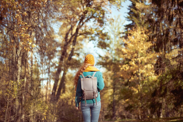 A young red-haired woman walks through the autumn park. A girl with lush curly hair looks at the autumn forest