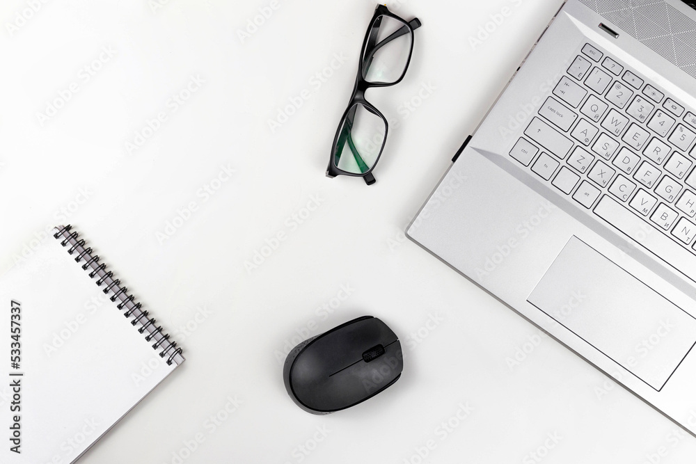 Poster A blank notebook with glasses a computer mouse and a laptop are on a white table. Top view with copy space