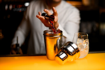 close-up of shaker into which hand of bartender pours liquid from steel jigger