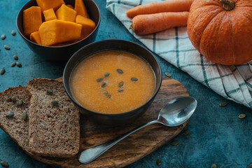 Pumpkin cream soup in a bowl with a spoon on wooden board on the table next to pumpkin whole and cut into pieces.  Healthy, vegetarian food. Diet. Home cooking. Thanksgiving day. Halloween.