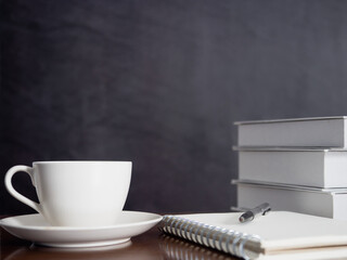 Coffee cup with notebook and pen on wood table dark background