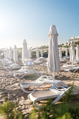 Rows of folded beach parasols and empty loungers on the background of sand and sea. Resort hotel. End of tourist season concept.