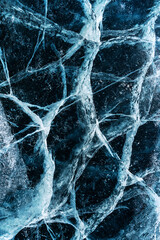 Transparent dark blue ice of frozen Baikal lake with white cracks pattern. Beautiful winter nature background.