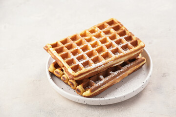 Fresh homemade sweet belgian waffles with honey and powdered sugar on round plate