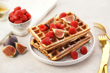 Fresh homemade sweet belgian waffles with honey, powdered sugar with fresh raspberries and figs on white plate