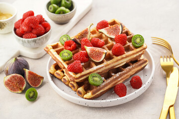 Fresh homemade sweet belgian waffles with honey, powdered sugar with fresh raspberries, kiwi berries and figs on white plate
