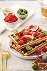 Fresh homemade sweet belgian waffles with honey, powdered sugar with fresh raspberries, kiwi berries and figs on white plate
