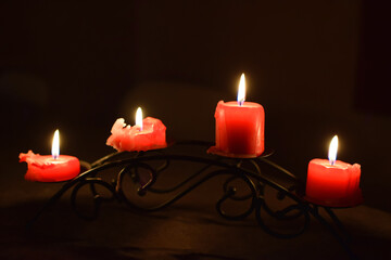 Four red candles burning in candlestick. Candle light in the dark.
