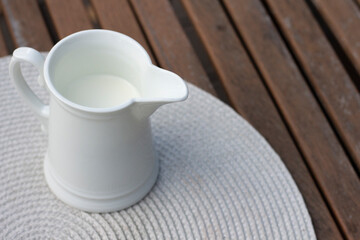White jug with milk on a wooden table. Breakfast on the veranda. Fresh drink, autumn leaves and...