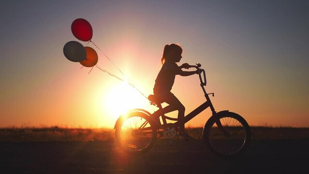 girl kid silhouette bike riding on a park. kid girl rides a bike in nature in the park on the road. happy family kid dream concept. daughter plays a bike rides on lifestyle a sandy road