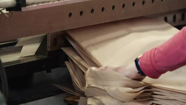 Ecological bags coming to the end of the manufacturing line. Labourer collecting the manufactured ecological bags from the conveyor equipment. Finishing the manufacturing of ecological shopping bags.