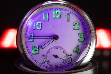 An old pocket watch with dangerous radioactive fluorescent paint. Scratches on the glass. Silver chrome metal. Black background. Violet light and green glow of numbers.