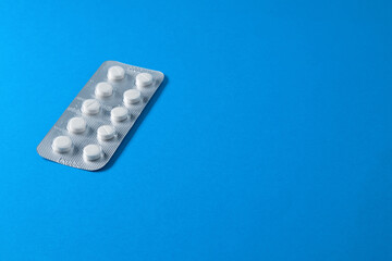 White tablets in a blister pack on a blue background with free space for text, copy space