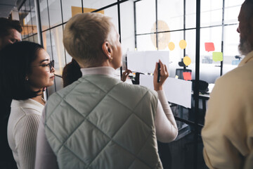 Group of colleagues attaching papers to glass wall in modern office