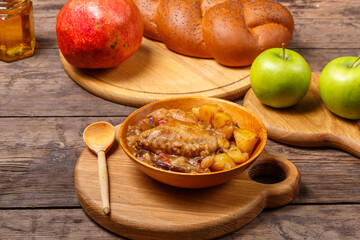 Chelnt with chicken in a wooden plate with a wooden spoon on the festive table for Rosh Hashanah next to challah honey and apples with pomegranate.
