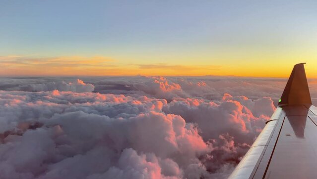 View out of airplane window of wing above puffy clouds with a colorful sunset. 4K UHD video footage