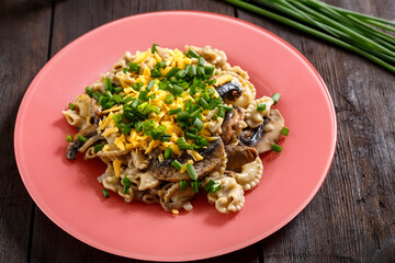 Pasta in a creamy sauce with mushrooms in a plate on the table next to green onion feathers.