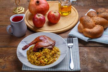 Spelled with vegetables and duck leg in a plate next to challah, wine, honey and apples with pomegranate for the Rosh Hashanah meal.