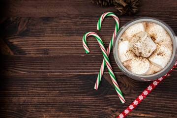 Hot chocolate with marshmallow and coco powder, candy cane pine cones, ribbon, pine needles, pine branch, dark wood, Christmas concept, top view, copy space.