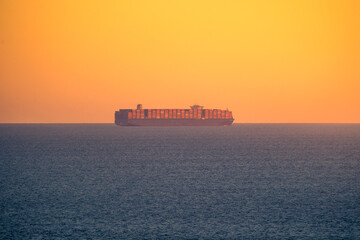 Sailing cargo ship in sea at sunset