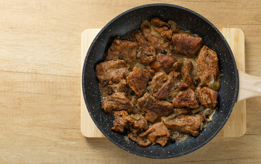 Pieces of fried beef with onions and spices in a frying pan on a brown table.Beef steak. Delicious lunch. copy space.