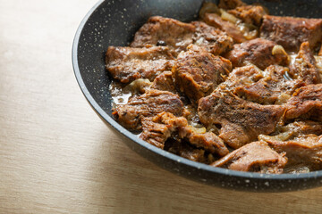 Pieces of fried beef with onions and spices in a frying pan on a brown table.Beef steak. Delicious lunch. copy space.