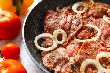 Fresh raw beef steaks with tomatoes, onions and peppers on a frying pan. Roast beef.