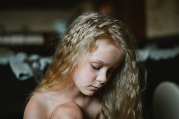 close-up portrait of a pensive, sad little girl with long curly hair at home - obrazy, fototapety, plakaty