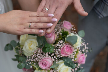Hände vom Brautpaar mit Eheringen auf Brautstrauß am Hochzeitstag als close-up