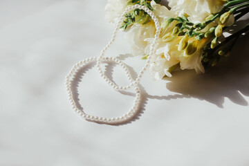 White bracelets with pearl beads on a white background with flowers.