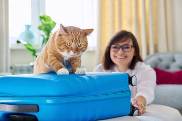 Sad ginger cat lying on suitcase of owner middle-aged woman