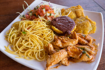 Plato combinado con pasta, ensalada, pollo y tostones con salsa de judías
