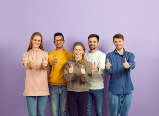 Portrait of smiling multiethnic young people isolated on violet background show thumbs up. Happy diverse multiracial teenagers recommend good training or internship. Recommendation concept.