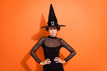 Photo portrait of lovely young girl hands waist irritated quarrel wear stylish black halloween witch garment isolated on orange background