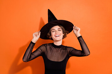 Fototapeta Photo of shiny dreamy girl dressed black gothic dress arms headwear laughing empty space isolated orange color background obraz