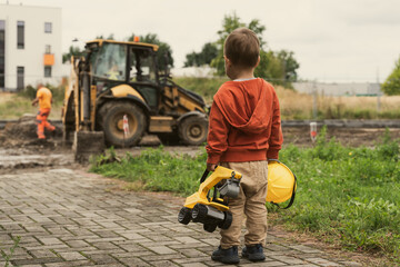 Child with excavator near construction site, dreams to be an engineer. Little builder. Education, and imagination, purposefulness concept - 533496312