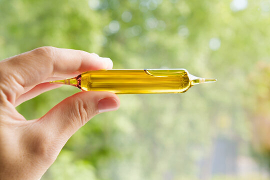 A hand holds an ampoule with liquid contents. Glass medicine vial mockup design. Medical dietary supplements. Vitamin complex. Production of a medicinal product close-up. Cosmetics elixir. Copy space