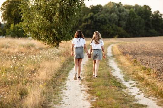 Two sisters holding their hands and walking on a path in the countryside at fall