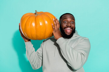Portrait of attractive cheerful amazed guy holding big orange pumpkin isolated over bright teal...