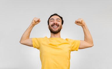 young latin man with braces smiles making a power gesture with his arms. white background
