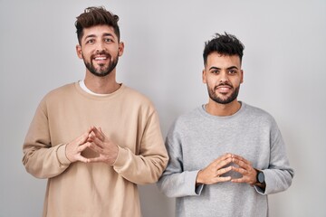 Young homosexual couple standing over white background hands together and fingers crossed smiling relaxed and cheerful. success and optimistic