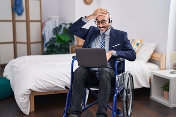 Hispanic man with beard sitting on wheelchair doing business video call stressed and frustrated with hand on head, surprised and angry face