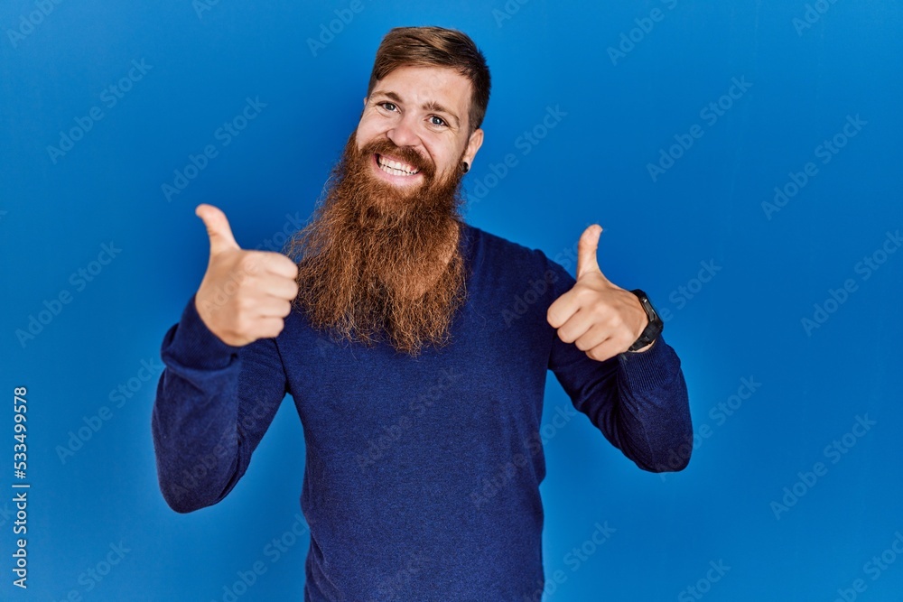 Sticker redhead man with long beard wearing casual blue sweater over blue background success sign doing posi