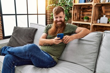 Obraz premium Young redhead man smiling confident using smartphone at home