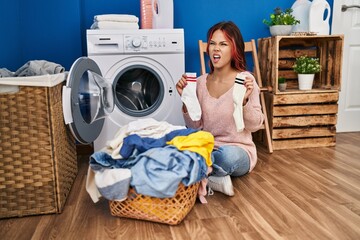 Young caucasian woman doing laundry holding socks angry and mad screaming frustrated and furious, shouting with anger. rage and aggressive concept.